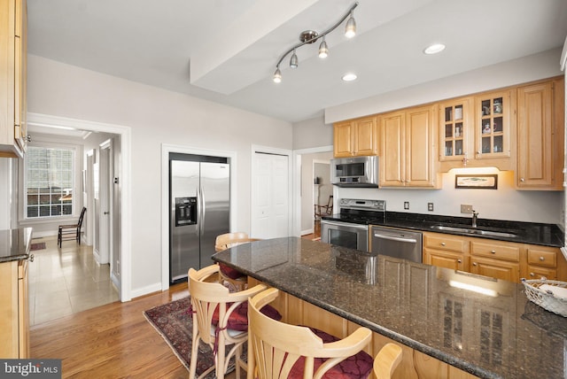 kitchen with appliances with stainless steel finishes, light wood-type flooring, kitchen peninsula, dark stone countertops, and a breakfast bar