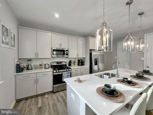 kitchen featuring sink, hanging light fixtures, tasteful backsplash, appliances with stainless steel finishes, and light wood-type flooring