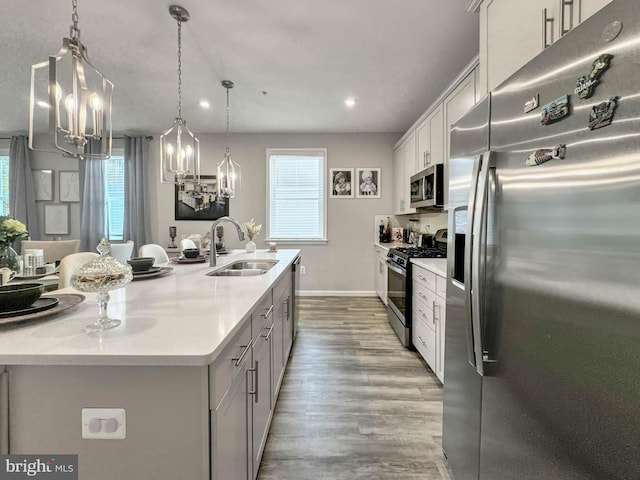 kitchen with appliances with stainless steel finishes, sink, decorative light fixtures, white cabinetry, and an island with sink