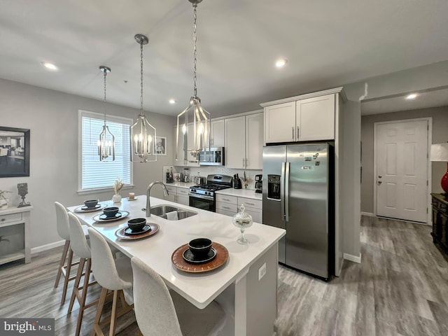 kitchen with appliances with stainless steel finishes, light wood-type flooring, sink, white cabinetry, and hanging light fixtures