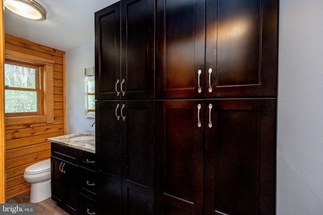 bathroom featuring toilet, vanity, and wooden walls