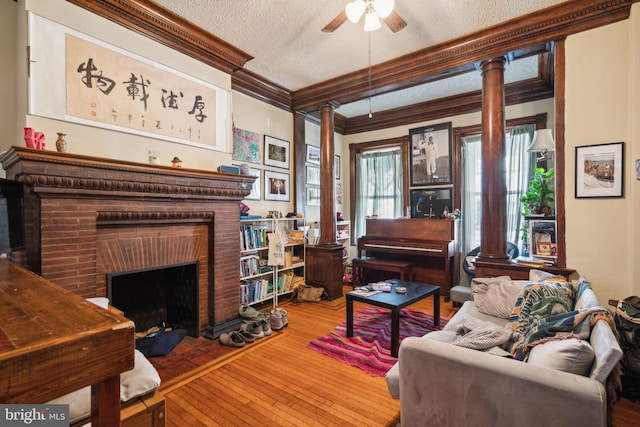 living room with a brick fireplace, hardwood / wood-style floors, a textured ceiling, ceiling fan, and crown molding