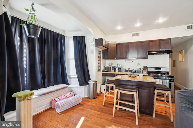 kitchen featuring light hardwood / wood-style floors, a center island, a kitchen breakfast bar, dark brown cabinets, and appliances with stainless steel finishes