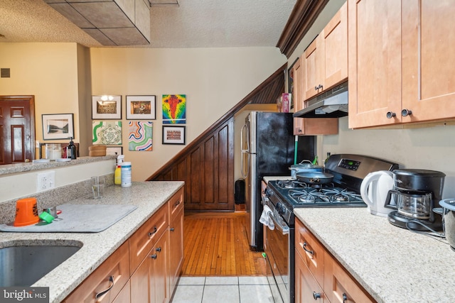 kitchen featuring stainless steel range with gas stovetop, a textured ceiling, light stone counters, and light hardwood / wood-style flooring