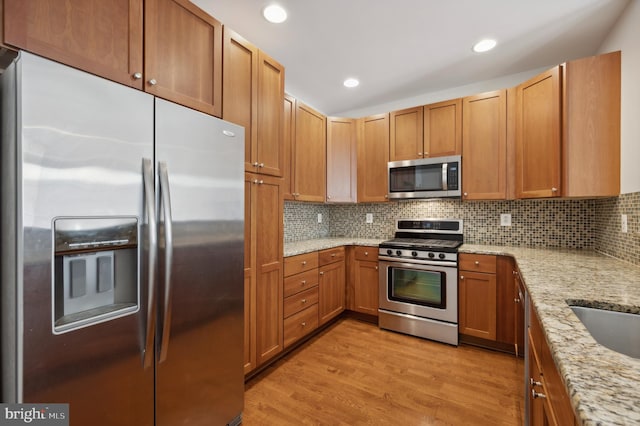 kitchen featuring tasteful backsplash, light wood-type flooring, appliances with stainless steel finishes, and light stone counters