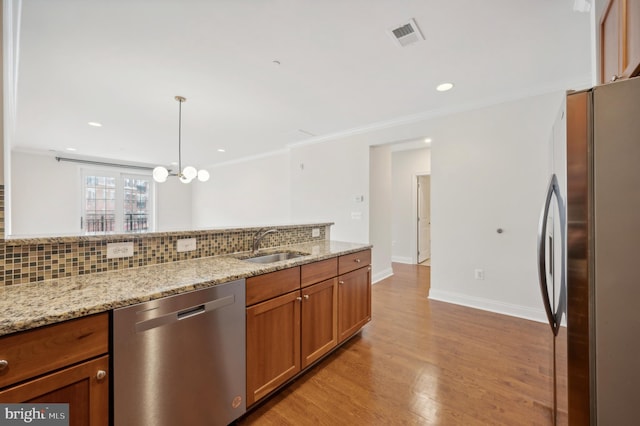 kitchen featuring stainless steel appliances, light hardwood / wood-style floors, tasteful backsplash, light stone countertops, and decorative light fixtures