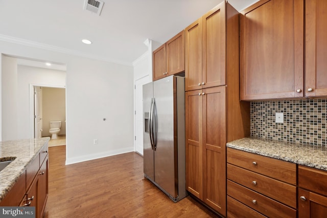 kitchen featuring tasteful backsplash, ornamental molding, stainless steel refrigerator with ice dispenser, light stone countertops, and light wood-type flooring