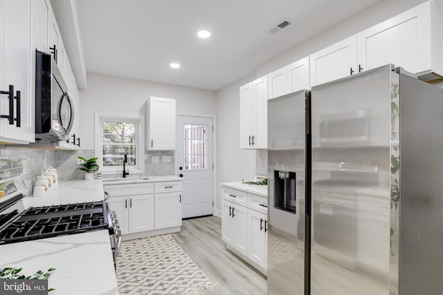 kitchen featuring tasteful backsplash, light wood-type flooring, white cabinetry, stainless steel appliances, and light stone counters