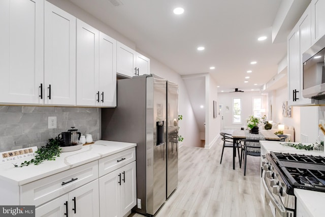 kitchen featuring appliances with stainless steel finishes, decorative backsplash, white cabinets, and light wood-type flooring