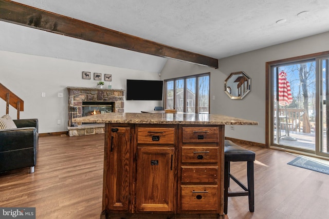 kitchen with a kitchen breakfast bar, a center island, lofted ceiling with beams, light stone counters, and light hardwood / wood-style floors