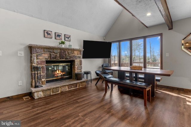 dining area with dark wood-type flooring, a stone fireplace, a textured ceiling, and lofted ceiling with beams