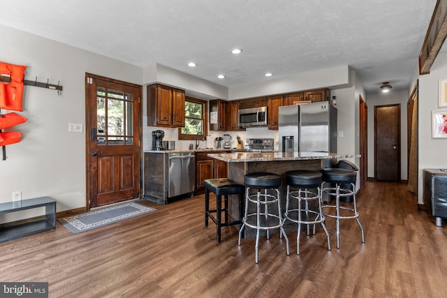 kitchen featuring appliances with stainless steel finishes, a center island, a kitchen bar, and dark hardwood / wood-style flooring