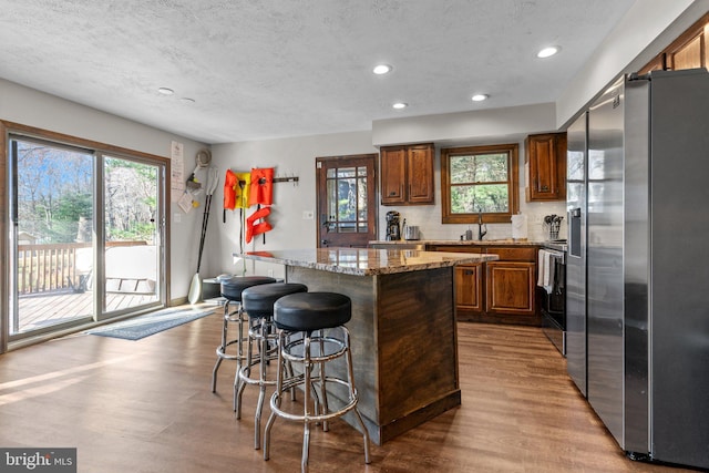 kitchen featuring appliances with stainless steel finishes, a center island, light hardwood / wood-style floors, light stone counters, and decorative backsplash