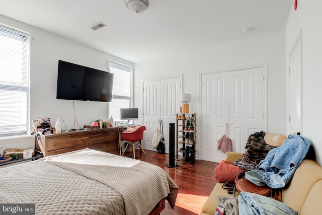 bedroom featuring multiple windows, two closets, and dark hardwood / wood-style flooring