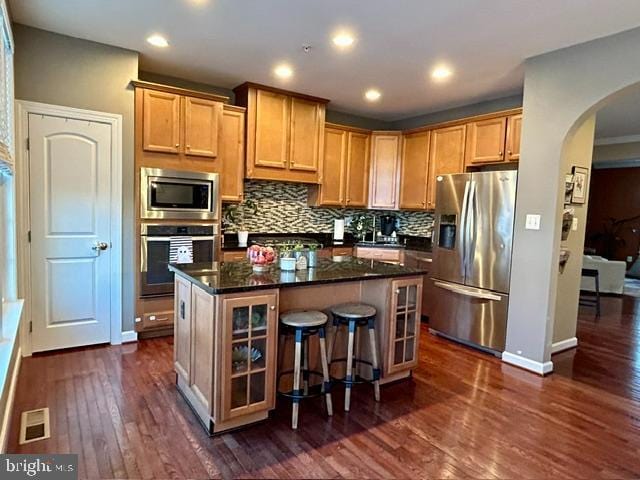 kitchen featuring a center island, dark hardwood / wood-style floors, dark stone countertops, tasteful backsplash, and stainless steel appliances