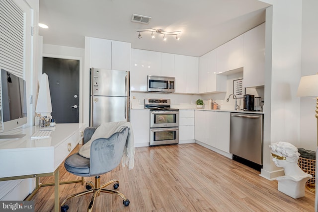 kitchen with appliances with stainless steel finishes, light hardwood / wood-style flooring, white cabinetry, and sink