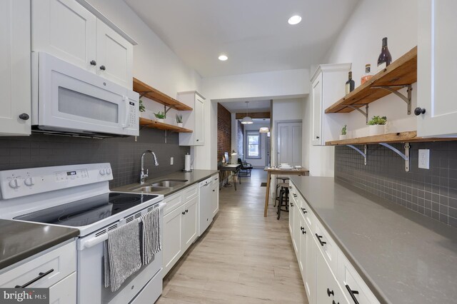 kitchen with white appliances, backsplash, white cabinetry, and sink