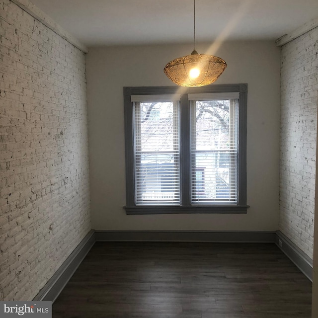 unfurnished dining area with dark wood-type flooring and brick wall