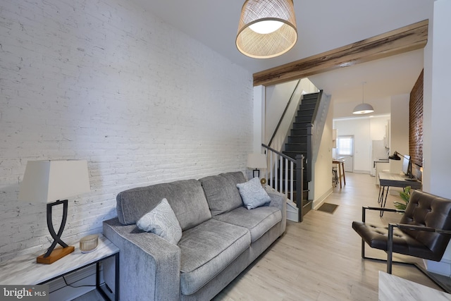 living room with beamed ceiling, light hardwood / wood-style floors, and brick wall