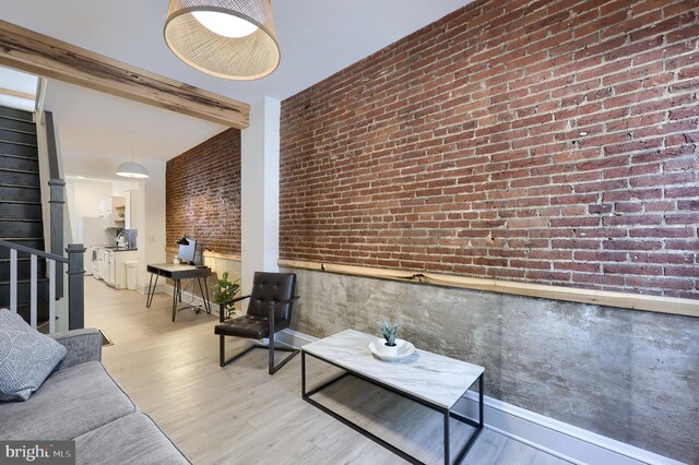 living room featuring light hardwood / wood-style flooring, beamed ceiling, and brick wall