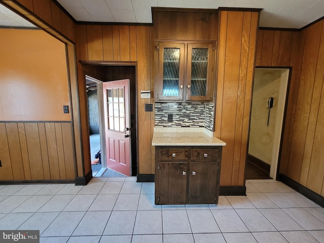 kitchen with tasteful backsplash, light stone countertops, light tile patterned flooring, and wooden walls