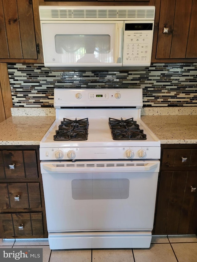 kitchen with light stone countertops, dark brown cabinets, and white appliances