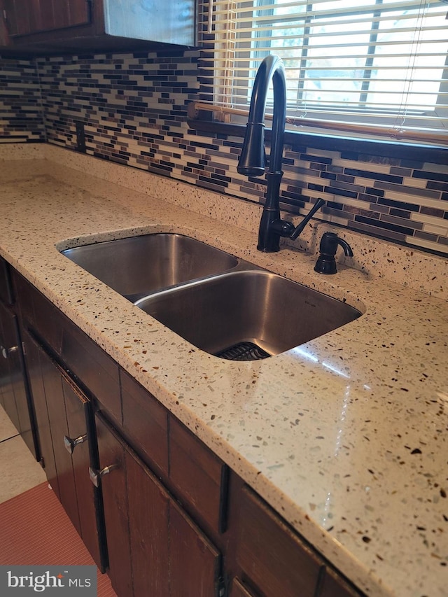 details featuring sink, light stone countertops, decorative backsplash, and dark brown cabinets