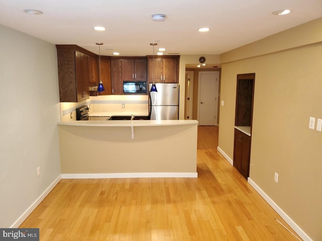 kitchen featuring kitchen peninsula, pendant lighting, stainless steel appliances, and light wood-type flooring