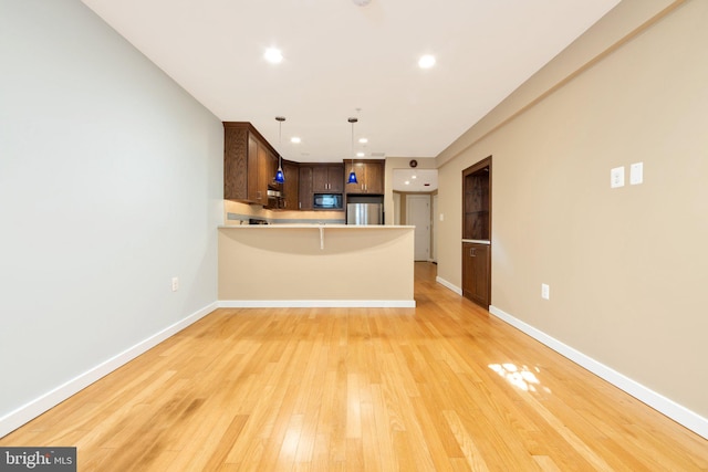 kitchen featuring stainless steel refrigerator, black microwave, light hardwood / wood-style flooring, kitchen peninsula, and pendant lighting