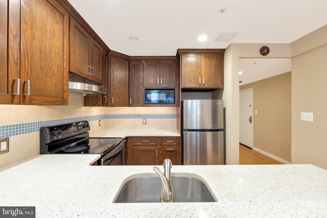 kitchen featuring backsplash, black appliances, sink, light wood-type flooring, and light stone counters