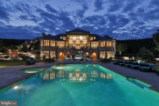 pool at dusk featuring an in ground hot tub and a patio area