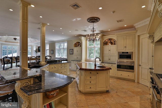 kitchen featuring a healthy amount of sunlight, ornate columns, a kitchen island with sink, and kitchen peninsula