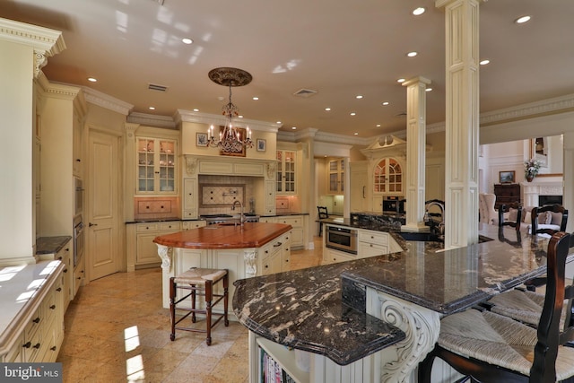 kitchen featuring dark stone counters, a breakfast bar area, decorative columns, ornamental molding, and a spacious island