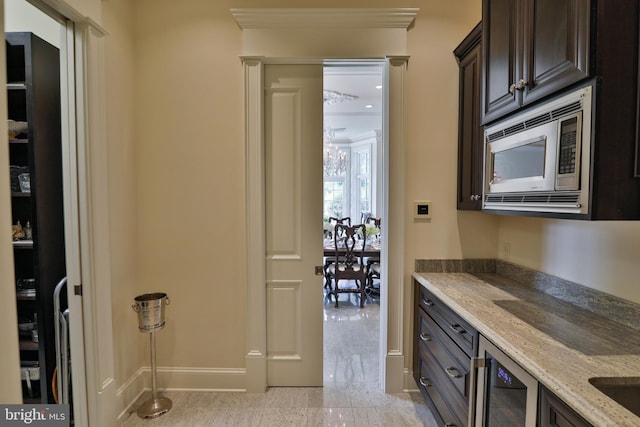 interior space with dark brown cabinetry, light stone countertops, beverage cooler, crown molding, and stainless steel microwave