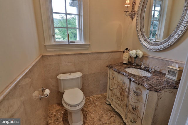 bathroom with toilet, vanity, tile walls, and a healthy amount of sunlight