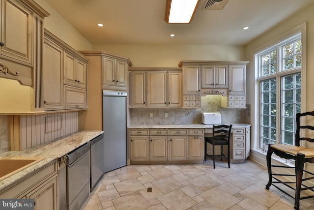 kitchen with black dishwasher, tasteful backsplash, stainless steel dishwasher, light stone countertops, and light brown cabinetry