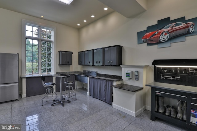 kitchen featuring a healthy amount of sunlight, stainless steel fridge, and a towering ceiling