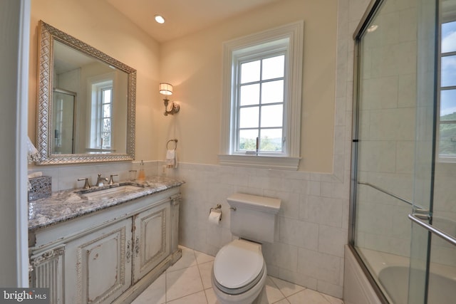 full bathroom featuring tile walls, shower / bath combination with glass door, vanity, tile patterned flooring, and toilet