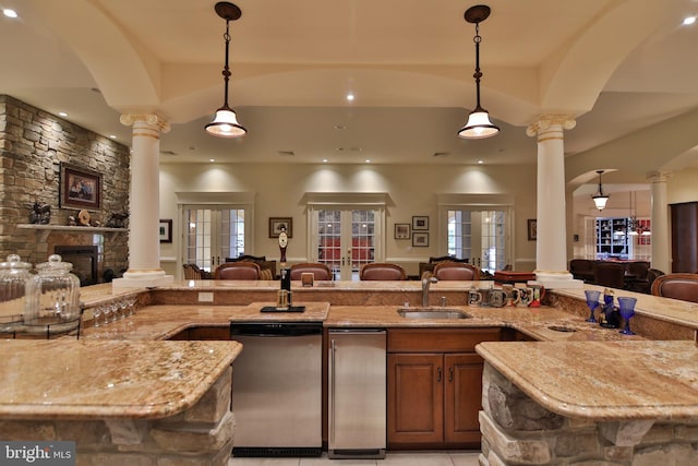 kitchen with stainless steel dishwasher, hanging light fixtures, sink, and decorative columns