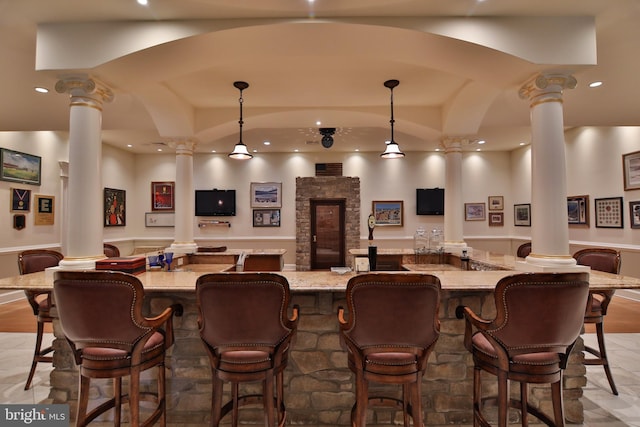 bar with hanging light fixtures, vaulted ceiling, ornate columns, and light stone counters