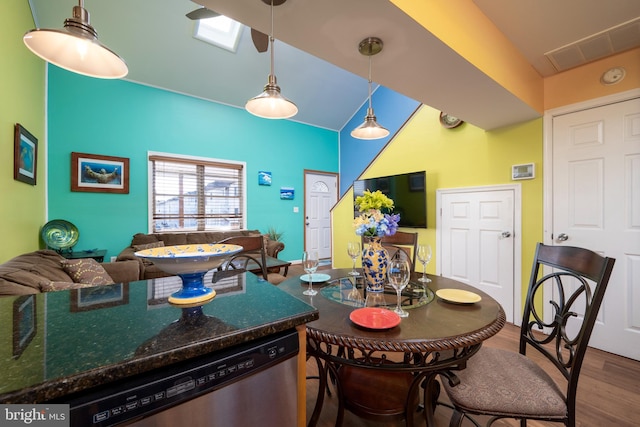 kitchen with hardwood / wood-style floors, lofted ceiling with skylight, dark stone counters, stainless steel dishwasher, and decorative light fixtures