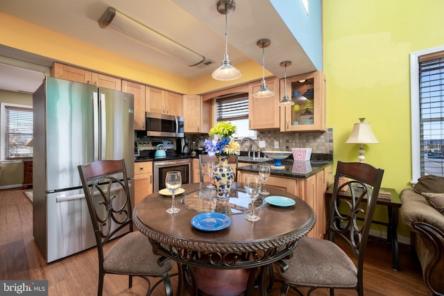 kitchen featuring decorative backsplash, light brown cabinetry, stainless steel appliances, wood-type flooring, and hanging light fixtures