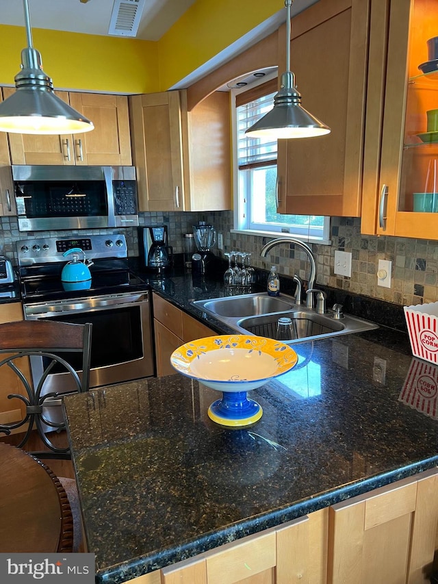 kitchen with backsplash, stainless steel appliances, dark stone counters, and sink