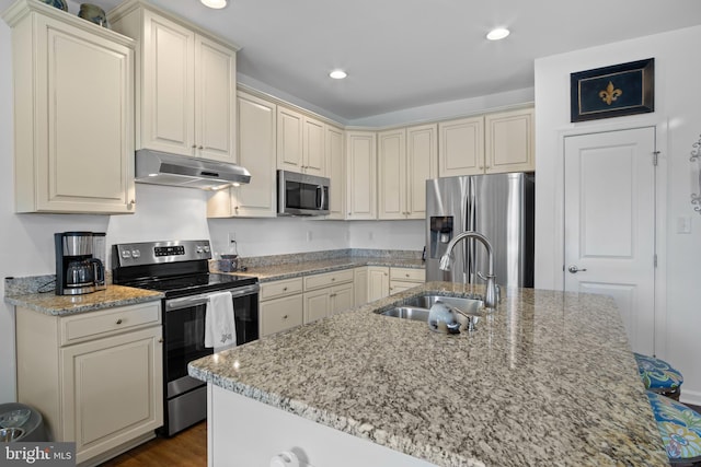 kitchen with light stone countertops, appliances with stainless steel finishes, sink, and a center island with sink