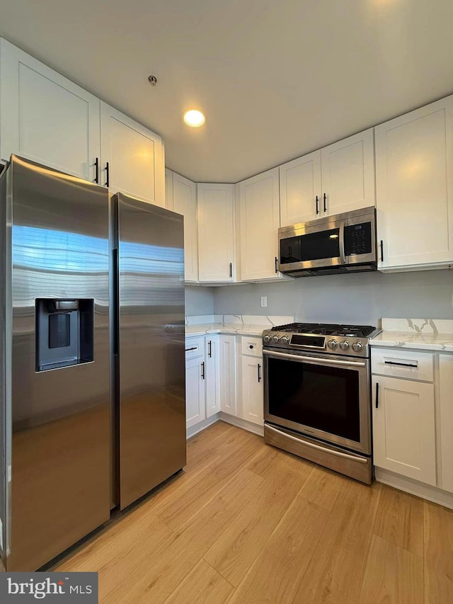 kitchen featuring white cabinets, stainless steel appliances, light stone countertops, and light hardwood / wood-style floors