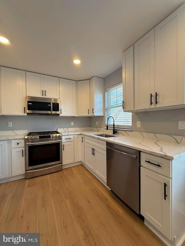 kitchen with white cabinets, sink, light wood-type flooring, appliances with stainless steel finishes, and light stone counters