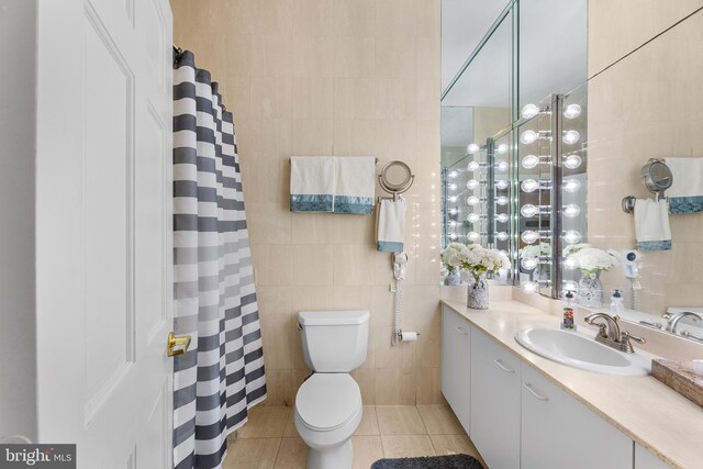 bathroom with toilet, vanity, tile patterned floors, and tile walls