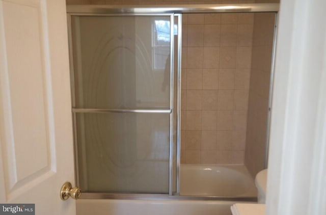 bathroom featuring combined bath / shower with glass door and toilet