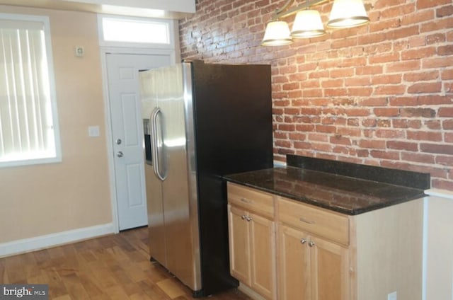 kitchen with light brown cabinets, light hardwood / wood-style flooring, hanging light fixtures, brick wall, and stainless steel fridge with ice dispenser