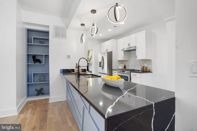 kitchen with white cabinetry, appliances with stainless steel finishes, decorative light fixtures, kitchen peninsula, and light hardwood / wood-style flooring